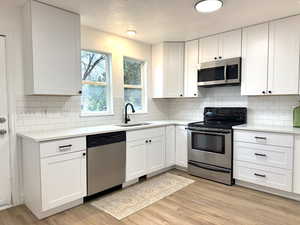 Kitchen with a sink, white cabinetry, light countertops, appliances with stainless steel finishes, and light wood finished floors