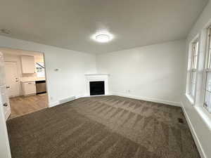 Unfurnished living room with baseboards, a fireplace, visible vents, and light colored carpet