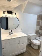 Full bath with shower / bathtub combination, toilet, vanity, a textured ceiling, and wood finished floors