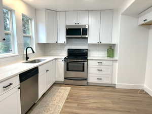 Kitchen featuring tasteful backsplash, white cabinets, appliances with stainless steel finishes, light wood-style floors, and a sink