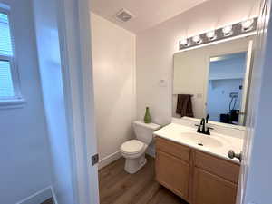 Bathroom featuring visible vents, toilet, vanity, wood finished floors, and baseboards