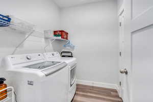 Clothes washing area with laundry area, washer and clothes dryer, wood finished floors, and baseboards