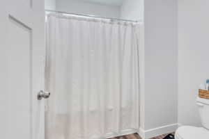 Bathroom featuring a shower with shower curtain, wood finished floors, toilet, and baseboards