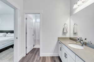 Full bathroom featuring connected bathroom, vanity, baseboards, and wood finished floors