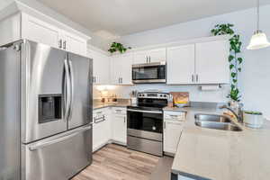 Kitchen with decorative light fixtures, stainless steel appliances, light wood-style floors, white cabinets, and a sink