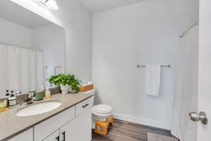 Full bath featuring toilet, wood finished floors, vanity, and baseboards