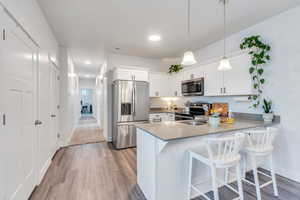 Kitchen with pendant lighting, appliances with stainless steel finishes, white cabinets, a peninsula, and a kitchen bar