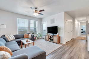 Living room with a textured ceiling, visible vents, baseboards, a ceiling fan, and light wood finished floors