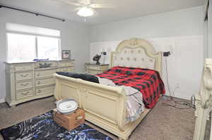 Bedroom featuring carpet, a decorative wall, ceiling fan, and wainscoting