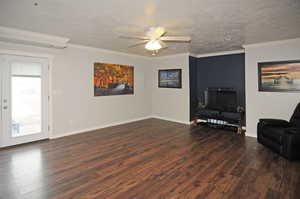 Living room featuring dark wood-style flooring, crown molding, ceiling fan, a textured ceiling, and baseboards