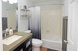 Bathroom featuring shower / tub combo with curtain, vanity, toilet, and wood finished floors