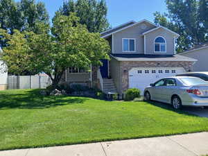 View of front facade featuring a garage, brick siding, a front yard, and fence