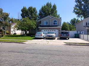 View of front of property featuring concrete driveway, stone siding, an attached garage, fence, and a front yard