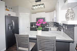 Kitchen featuring stainless steel appliances, a peninsula, a sink, white cabinets, and decorative light fixtures