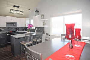 Kitchen with white cabinets, stainless steel microwave, decorative light fixtures, black electric range, and backsplash