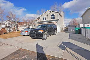 View of front of house with a chimney, concrete driveway, a storage shed, fence, and an outdoor structure