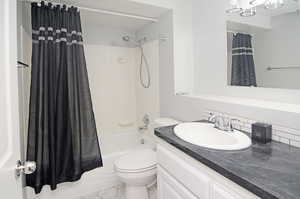 Bathroom featuring tile patterned flooring, shower / bathtub combination with curtain, toilet, and vanity