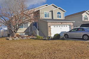 Traditional-style home with stairs, a front lawn, an attached garage, and brick siding