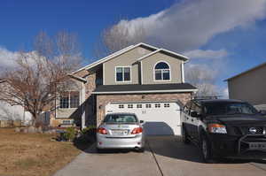 View of front facade with driveway, an attached garage, a shingled roof, and brick siding