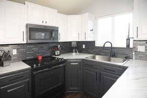 Kitchen featuring stainless steel microwave, black range with electric stovetop, a sink, and white cabinetry