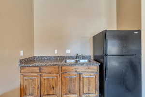 Kitchen with brown cabinetry, dark countertops, a sink, and freestanding refrigerator