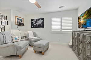 Living area featuring light carpet, baseboards, visible vents, and a ceiling fan