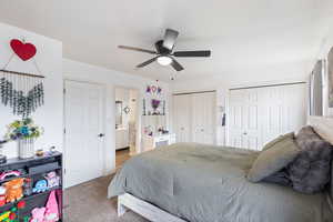 Carpeted bedroom with two closets, ceiling fan, and ensuite bathroom