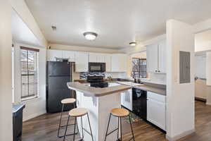 Kitchen featuring dark wood-type flooring, white cabinetry, electric panel, a center island, and black appliances