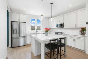 Kitchen featuring stainless steel appliances, a kitchen breakfast bar, white cabinets, hanging light fixtures, and light countertops