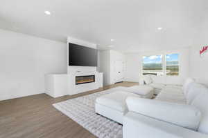 Living room with a glass covered fireplace, baseboards, recessed lighting, and wood finished floors