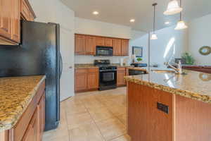 Kitchen featuring light tile patterned floors, a sink, hanging light fixtures, brown cabinets, and black appliances