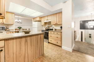 Kitchen featuring stainless steel appliances, light countertops, hanging light fixtures, an inviting chandelier, and light brown cabinets