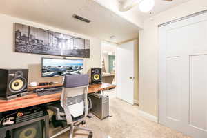 Office space featuring a textured ceiling, light speckled floor, visible vents, baseboards, and a ceiling fan