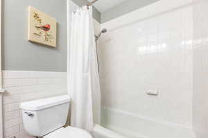 Full bath featuring shower / bath combination with curtain, a wainscoted wall, tile walls, and toilet