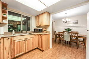 Kitchen with a sink, light wood-style floors, light countertops, hanging light fixtures, and stainless steel microwave