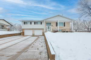 View of front facade with covered porch, brick siding, driveway, and an attached garage