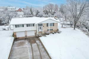 Snow covered house with a garage, driveway, brick siding, and a residential view