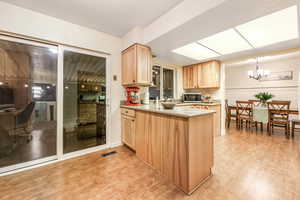 Kitchen with pendant lighting, light countertops, stainless steel microwave, and light brown cabinets