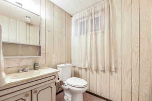 Half bathroom with toilet, wood walls, and vanity