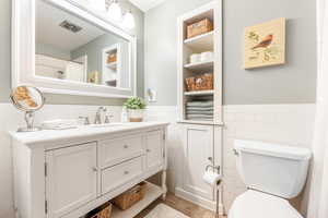 Full bath with visible vents, toilet, a wainscoted wall, vanity, and tile walls