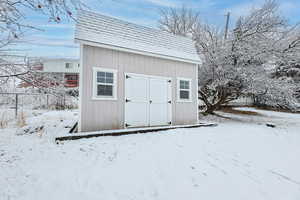 Snow covered structure featuring an outdoor structure, fence, and a storage shed