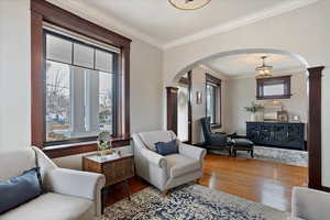 Living area with light wood-style floors, arched walkways, crown molding, and ornate columns