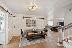 Dining room with light wood-style floors, a barn door, stairway, and a textured ceiling