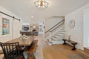 Dining room featuring a textured ceiling, a barn door, stairway, light wood-type flooring, and a brick fireplace