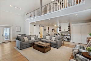 Family room with high vaulted ceiling, a barn door, recessed lighting, and light wood-style floors