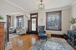 Sitting room featuring arched walkways, crown molding, baseboards, light wood finished floors, and an inviting chandelier