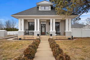 View of front of house with covered porch, roof with shingles, fence, and a front lawn