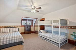 Bedroom with vaulted ceiling, a textured ceiling, light carpet, and a ceiling fan