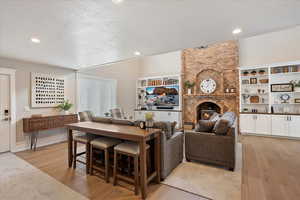 Family room area featuring a textured ceiling, a brick fireplace, recessed lighting, and light wood-style floors