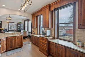 Kitchen with light stone counters, a sink, hanging light fixtures, and ornamental molding